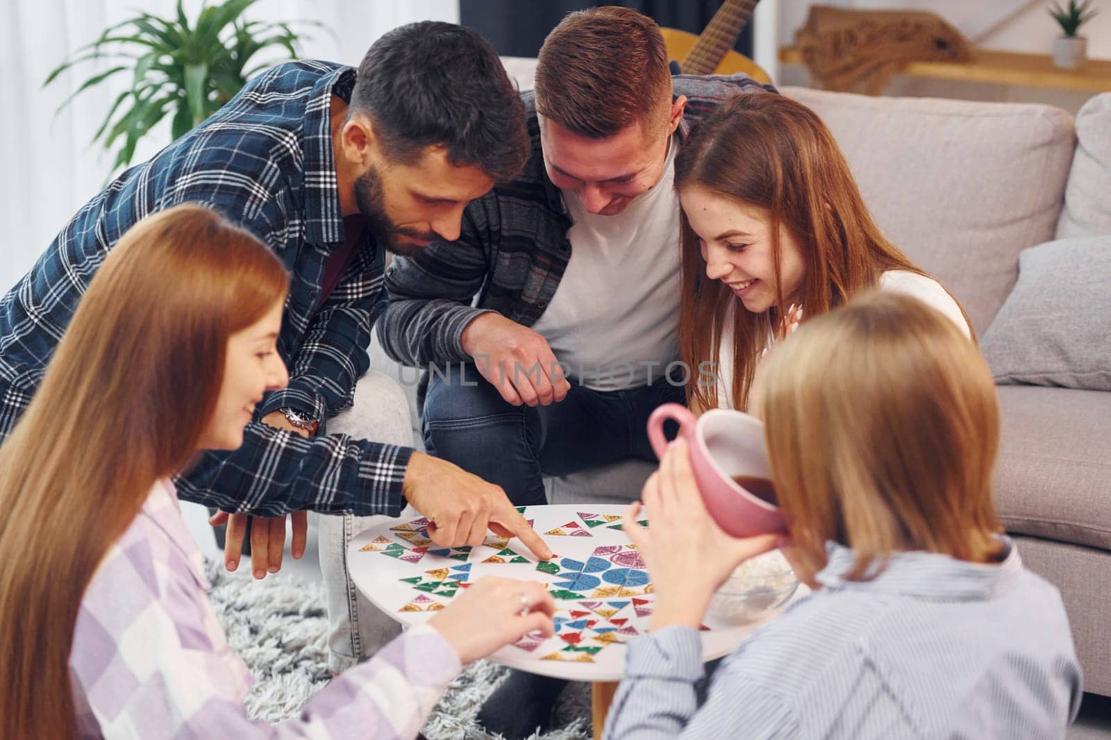 Playing puzzle game. Group of friends have party indoors together.