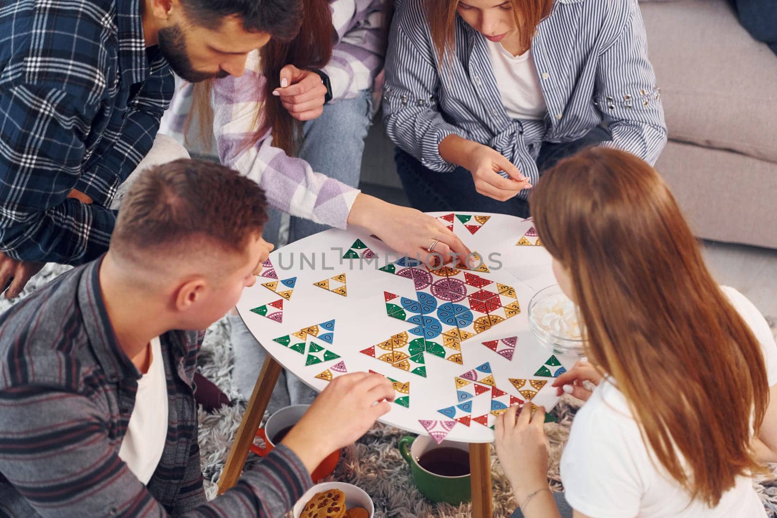 Focused at puzzle game. Group of friends have party indoors together.