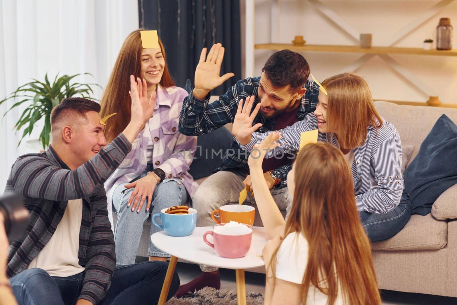 With stickers on forehead. Group of friends have party indoors together.