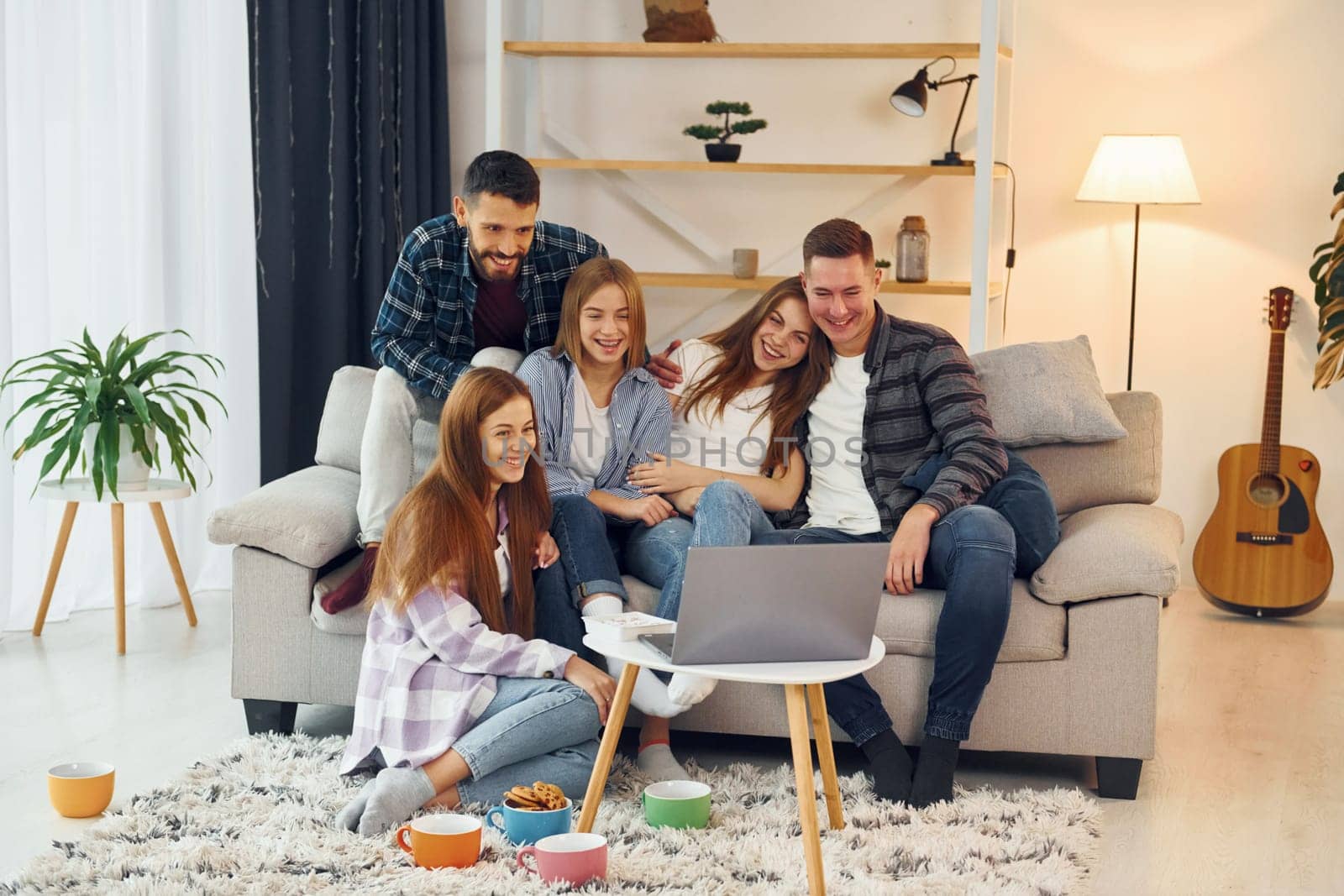 Using laptop. Group of friends have party indoors together.