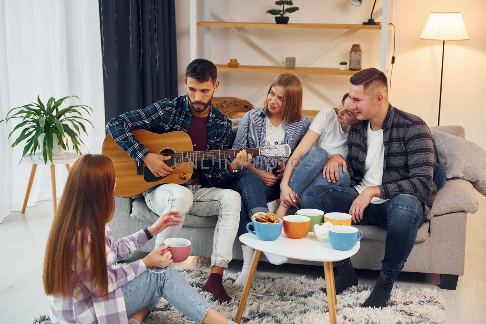 Playing acoustic guitar. Group of friends have party indoors together.