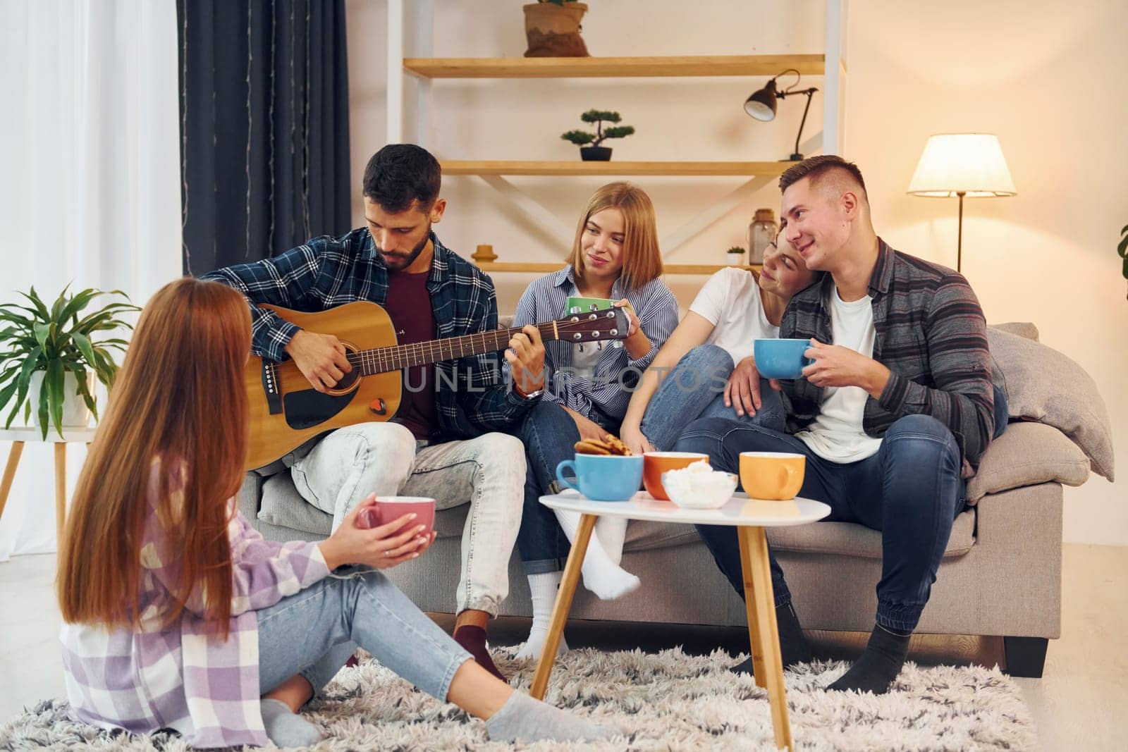 Playing acoustic guitar. Group of friends have party indoors together.