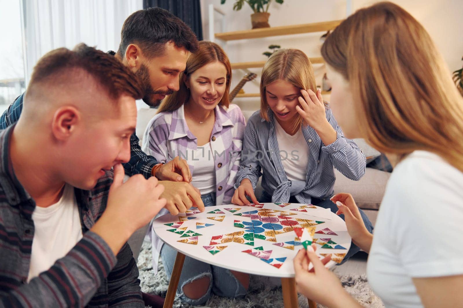 Puzzle game on the table. Group of friends have party indoors together.