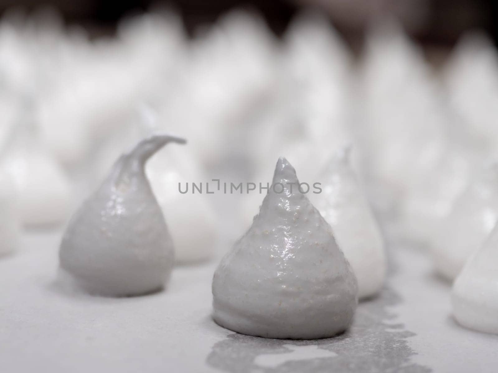 pastry chef baker artisan making white swirl and twirl meringue cones with piping bag filled with egg cream and sugar to bake for sweet preparation