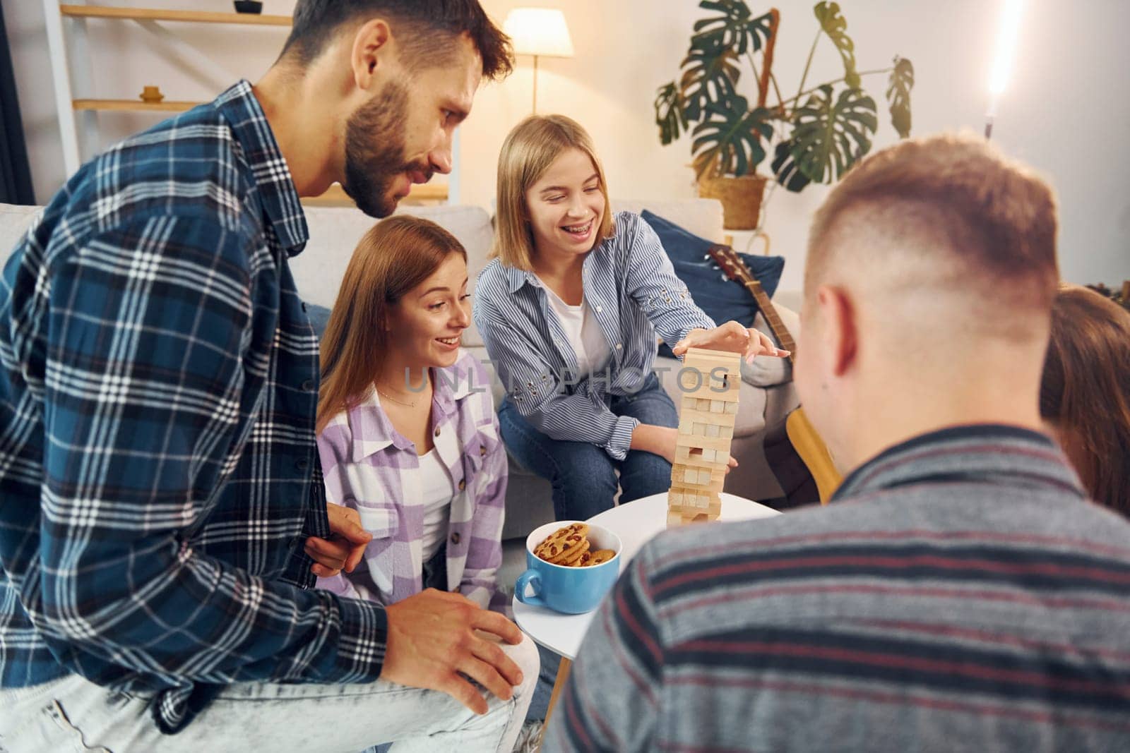 Focused on the tower building game. Group of friends have party indoors together.