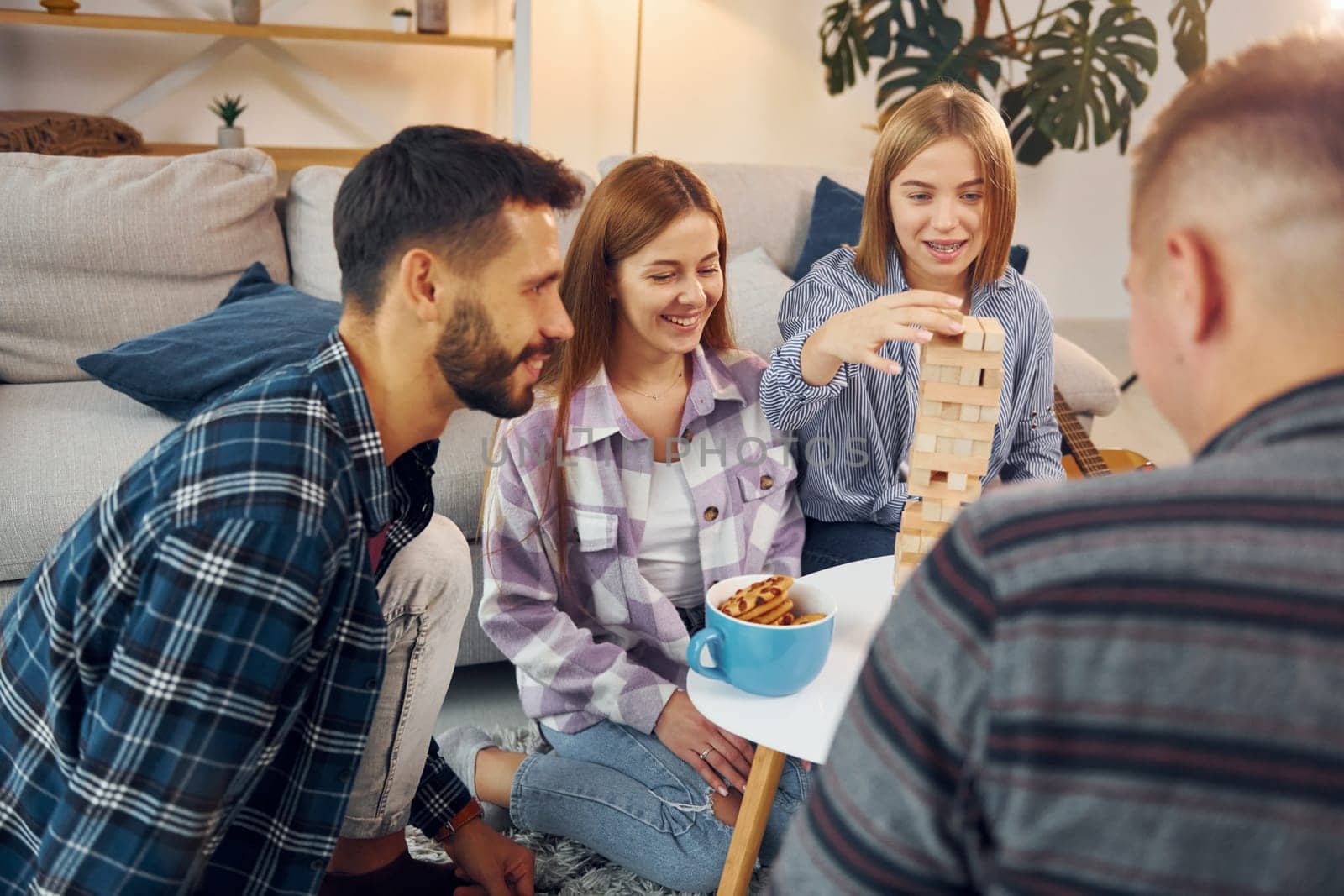 Focused on the tower building game. Group of friends have party indoors together.