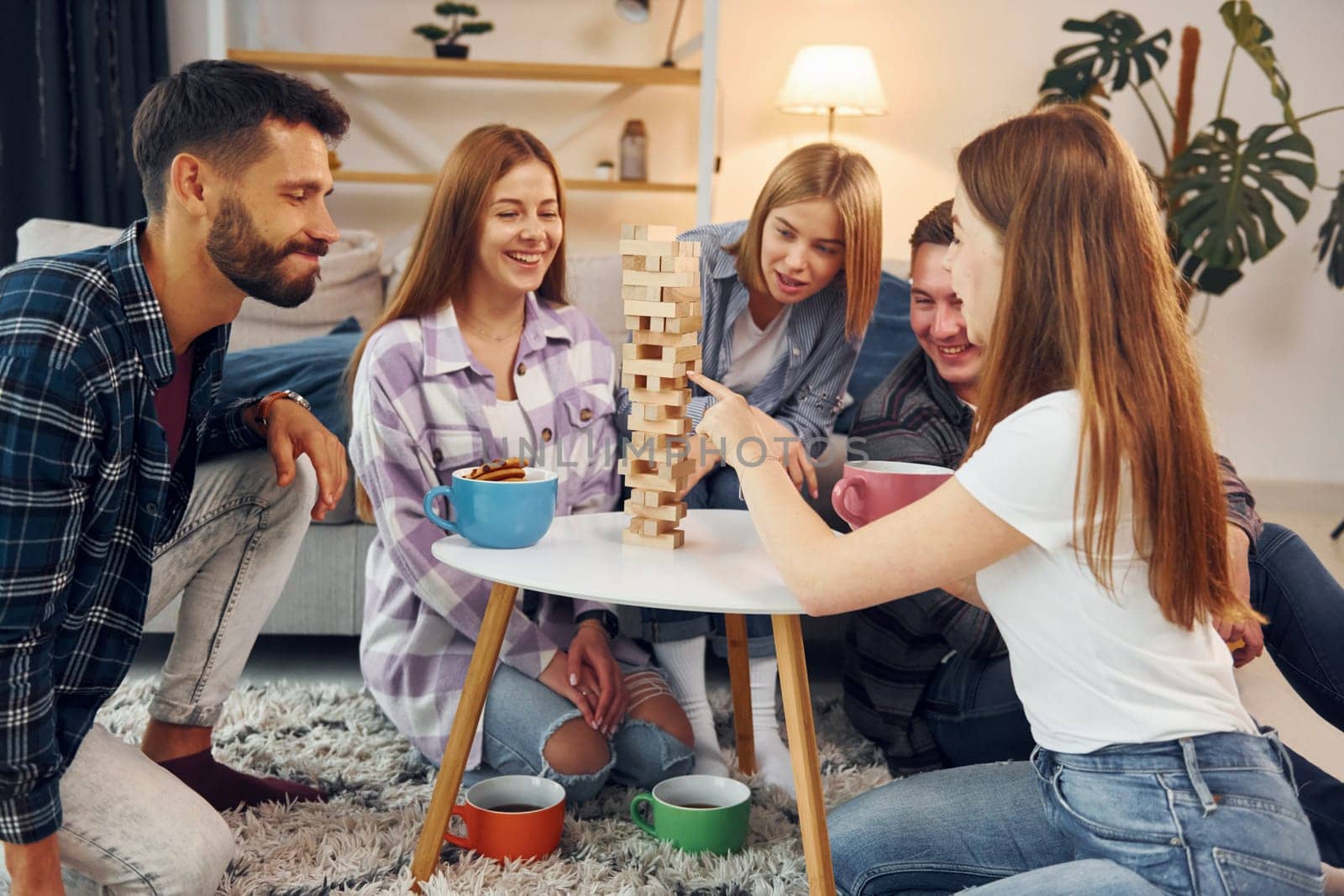 Wooden tower game on the table. Group of friends have party indoors together.