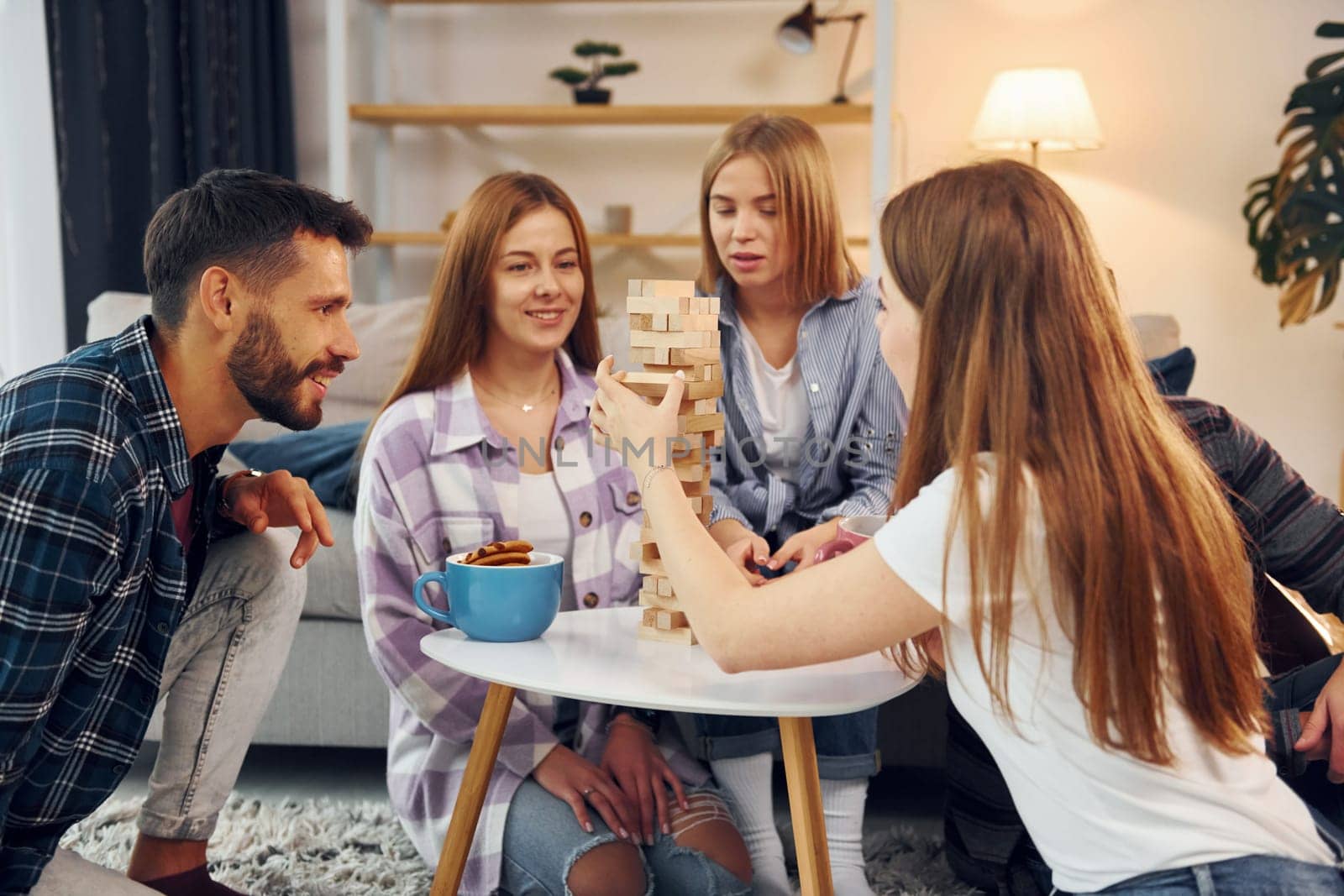 Wooden tower game on the table. Group of friends have party indoors together.