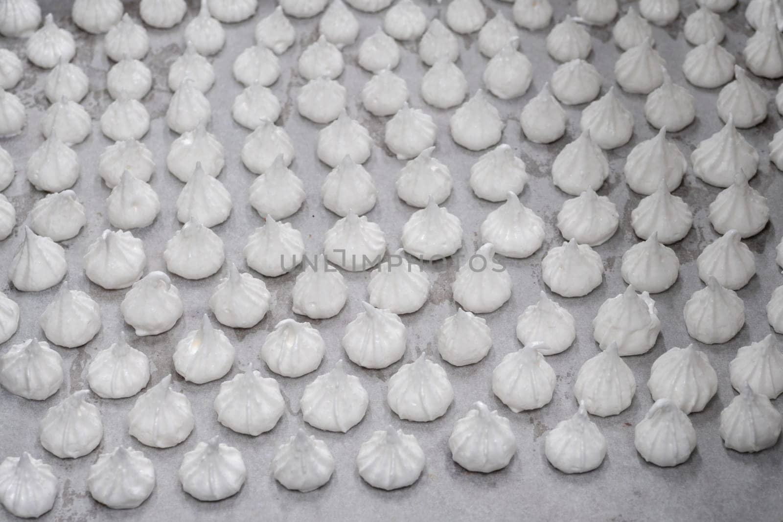 pastry chef baker artisan making white swirl and twirl meringue cones with piping bag filled with egg cream and sugar to bake for sweet preparation