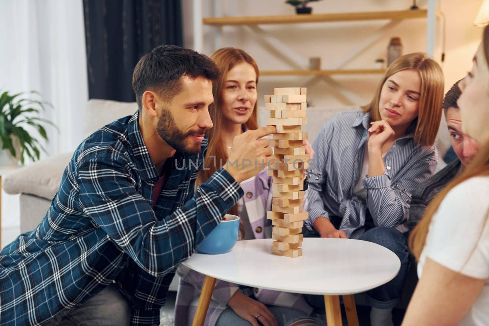 Playing wooden tower game. Group of friends have party indoors together.