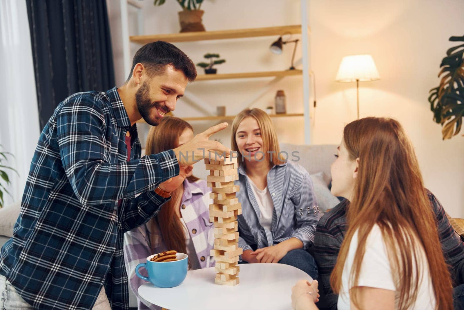 Wooden tower game on the table. Group of friends have party indoors together.