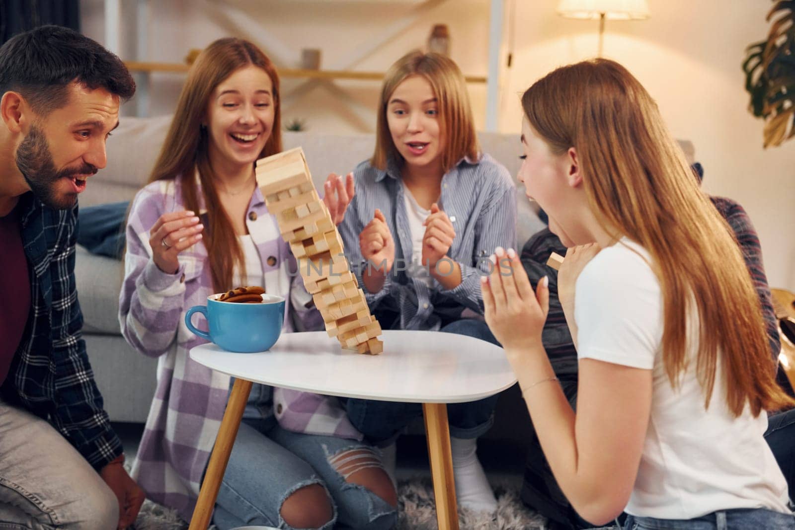 Wooden tower has fallen. Group of friends have party indoors together.