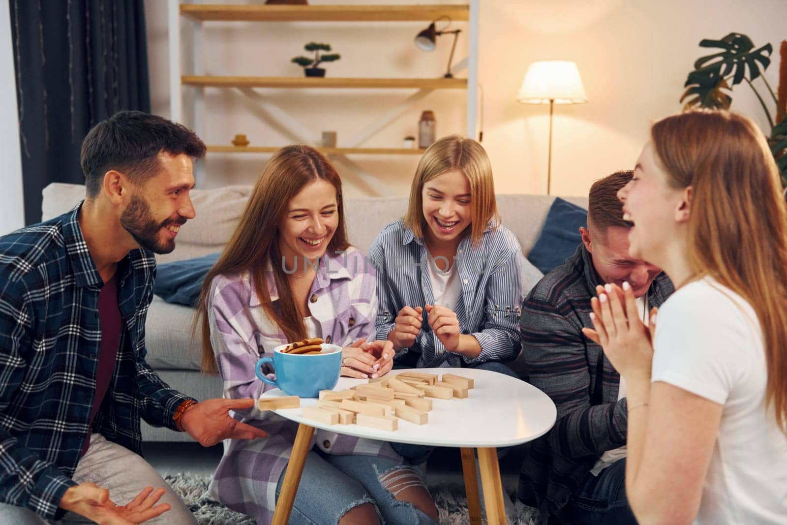 Wooden tower has fallen. Group of friends have party indoors together.