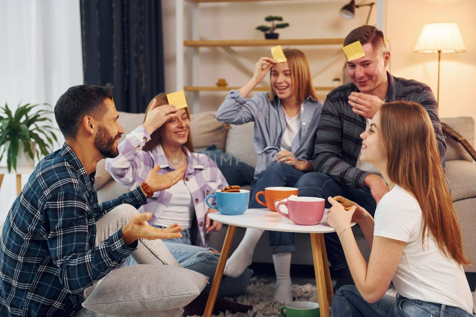 Yellow stickers on forehead. Group of friends have party indoors together.