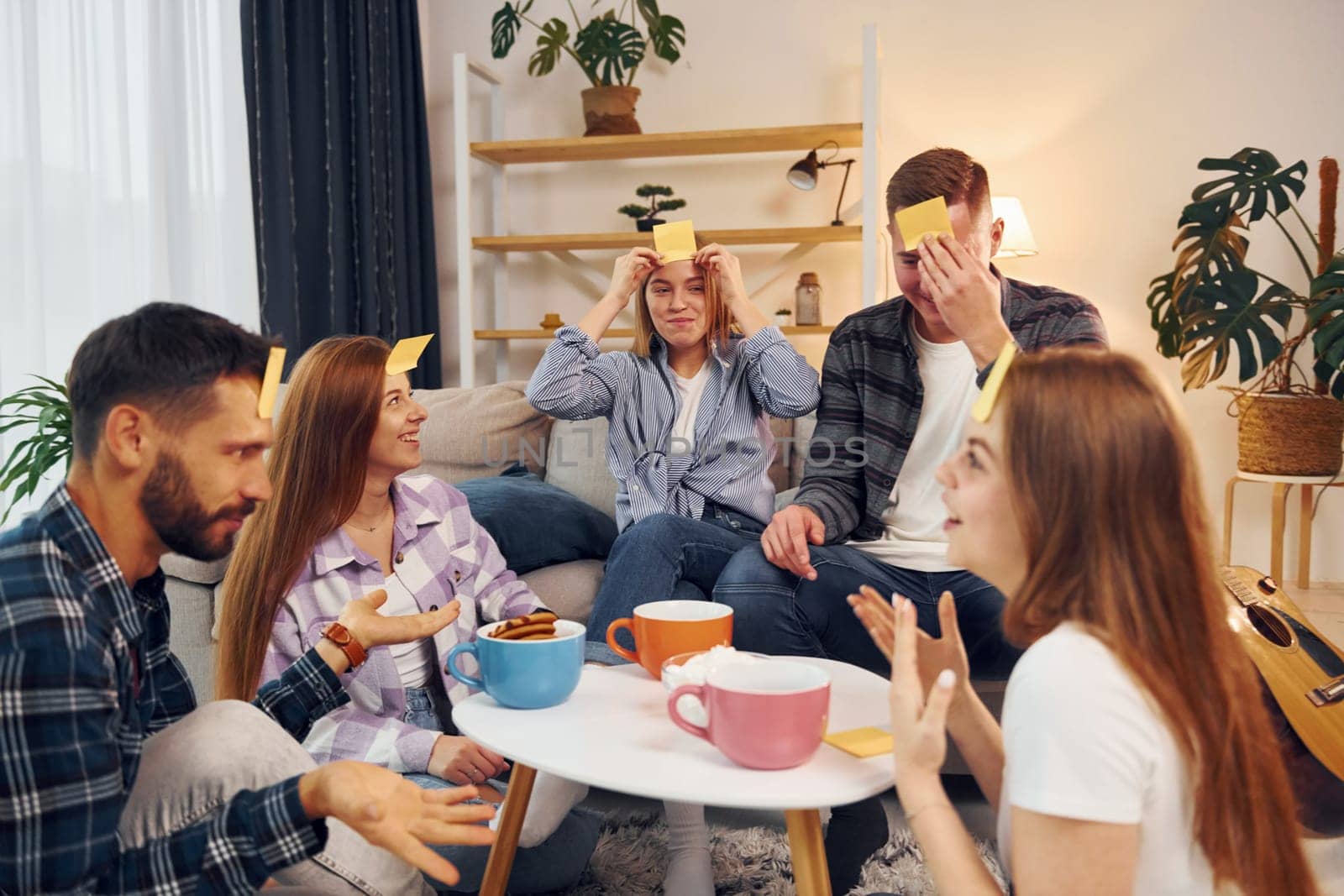 Yellow stickers on forehead. Group of friends have party indoors together.