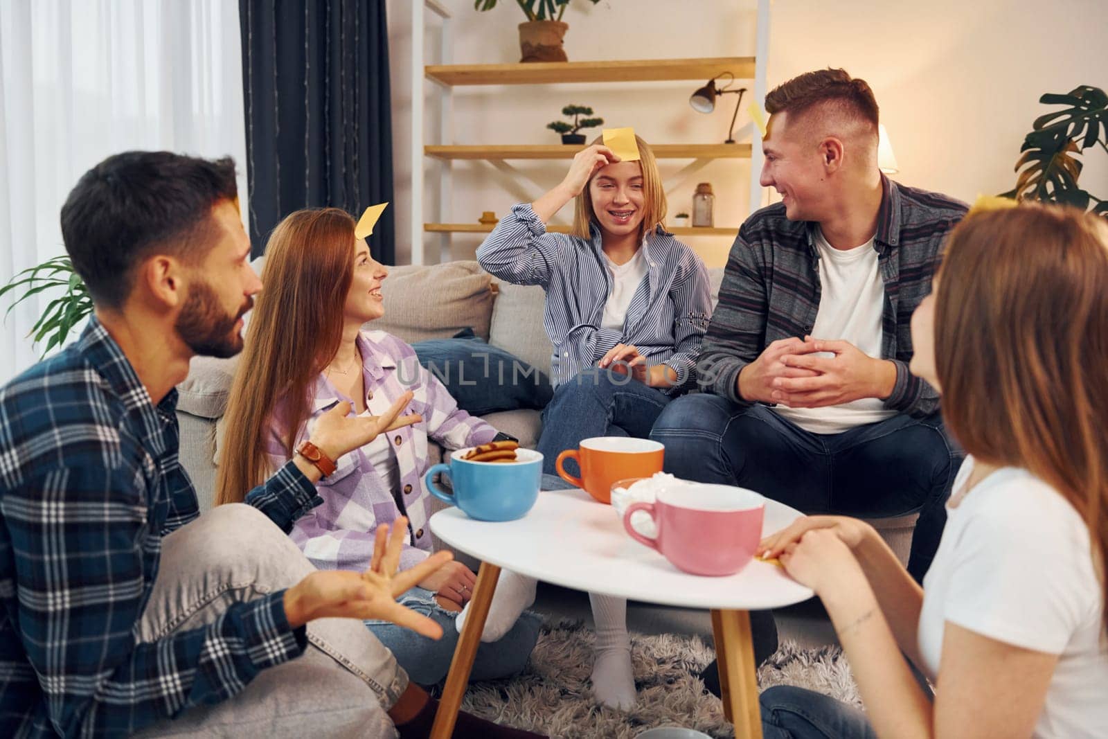 Yellow stickers on forehead. Group of friends have party indoors together.