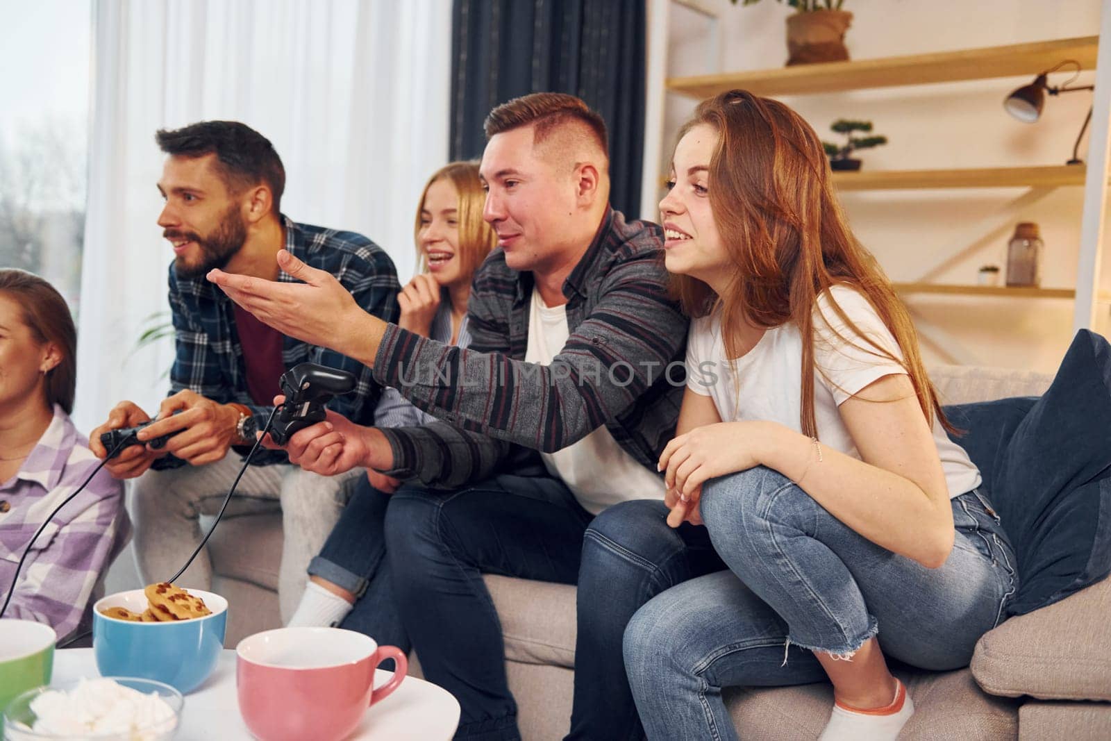 Playing video game. Group of friends have party indoors together.