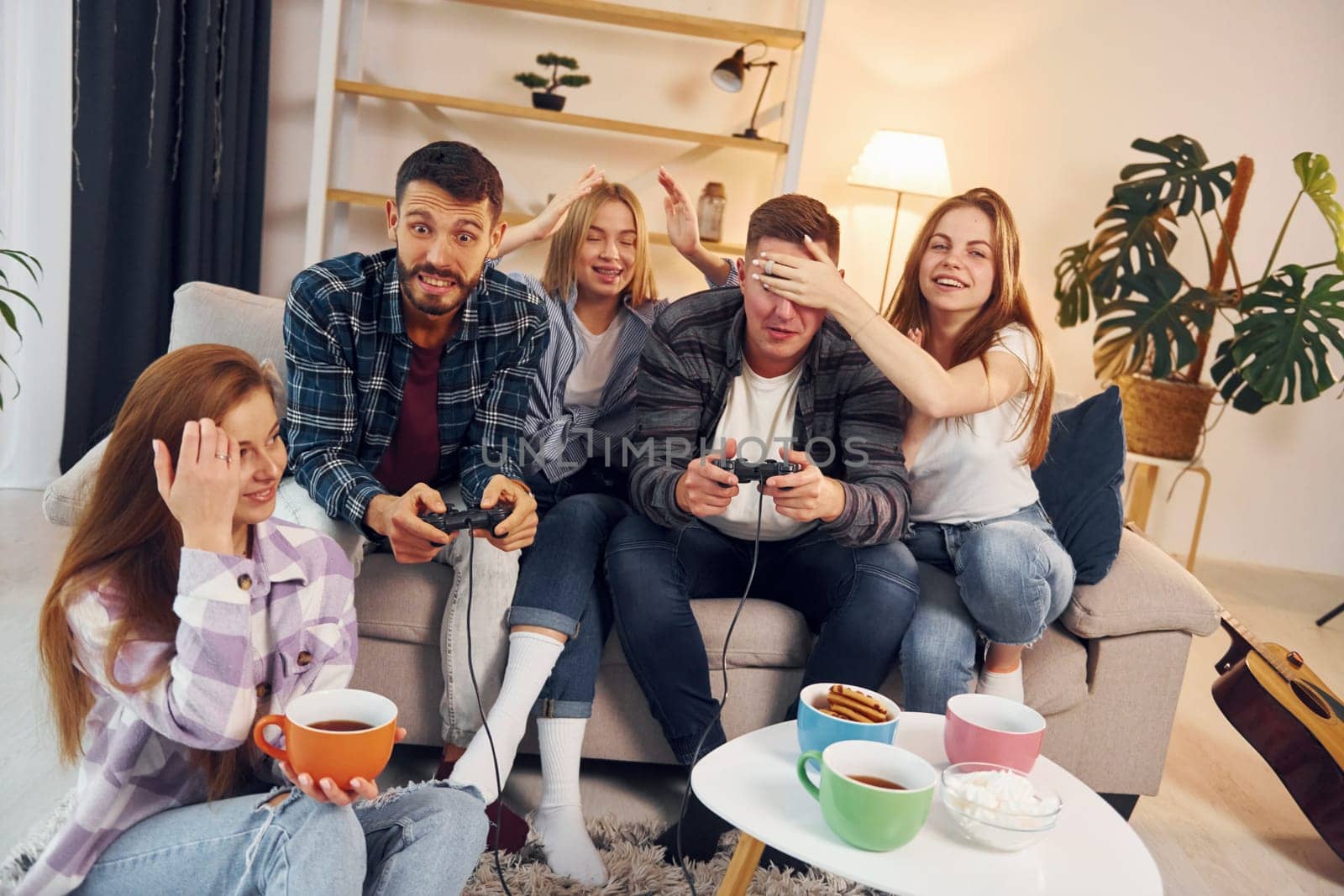 Playing video game. Group of friends have party indoors together.