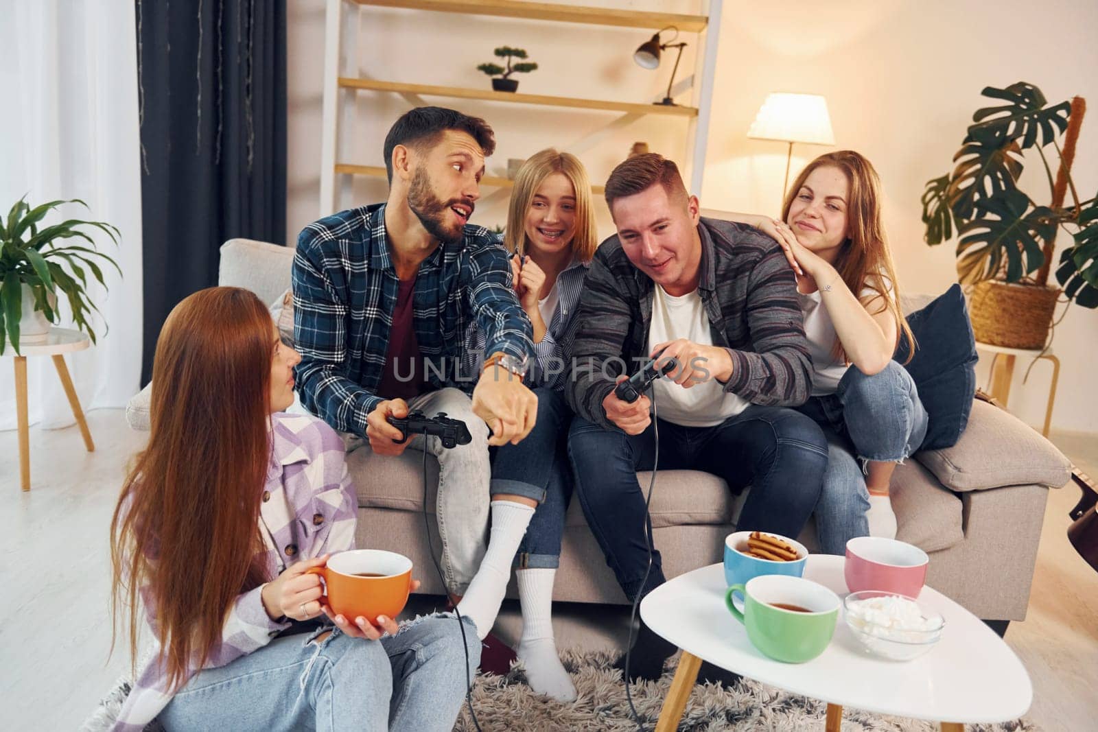 Playing video game. Group of friends have party indoors together.