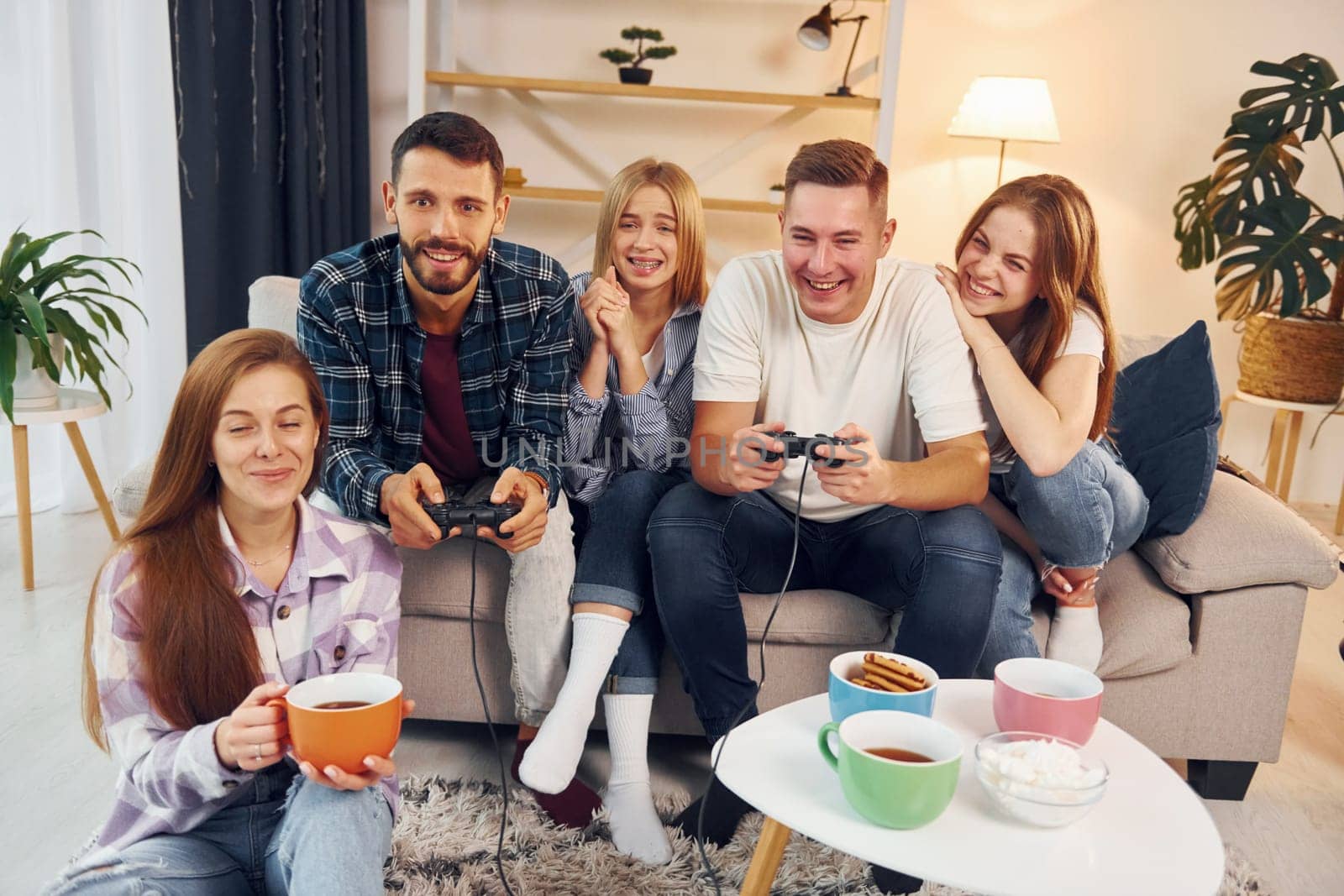 Using joysticks to play video game. Group of friends have party indoors together.