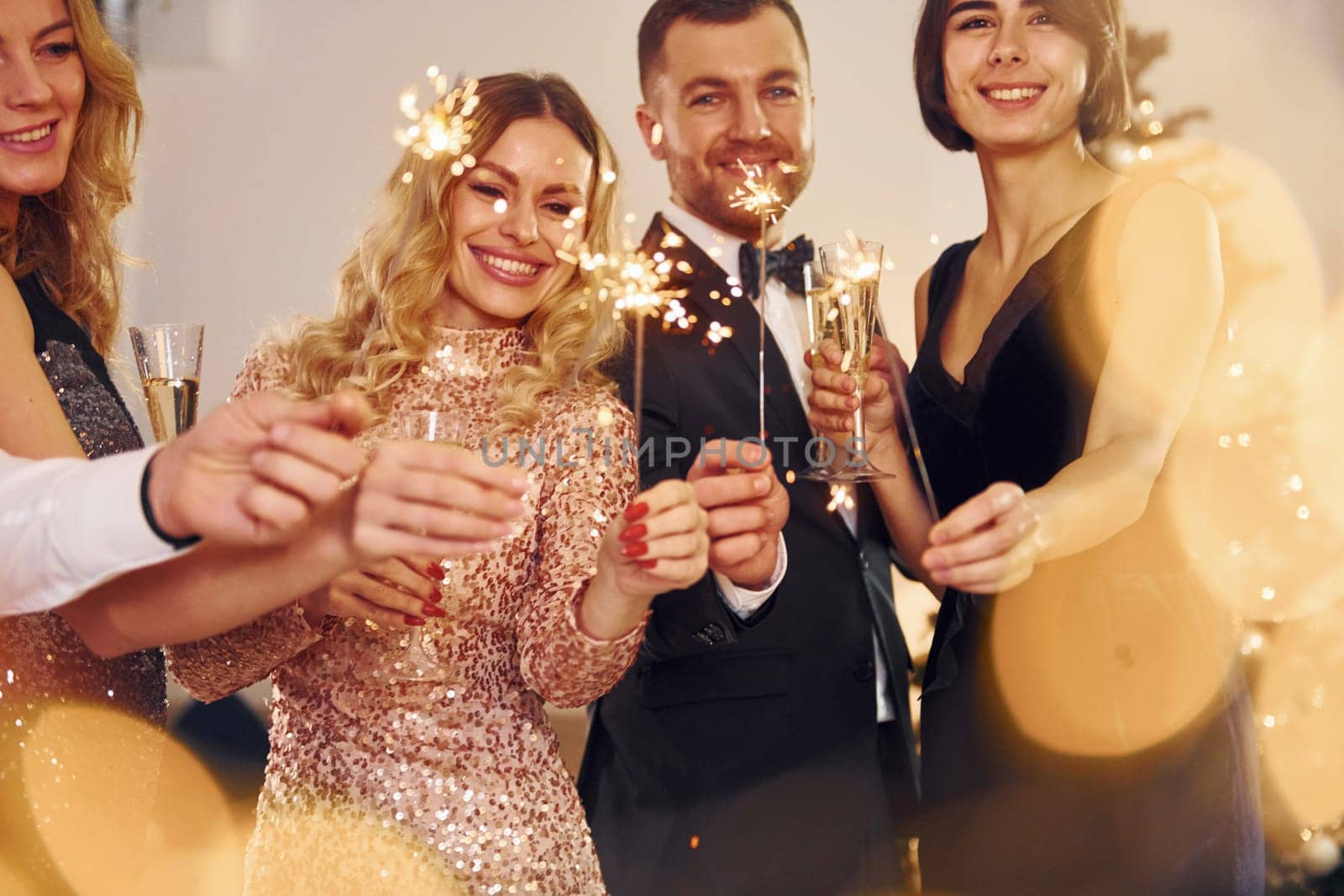 With sparklers in hands. Group of people have a new year party indoors together.
