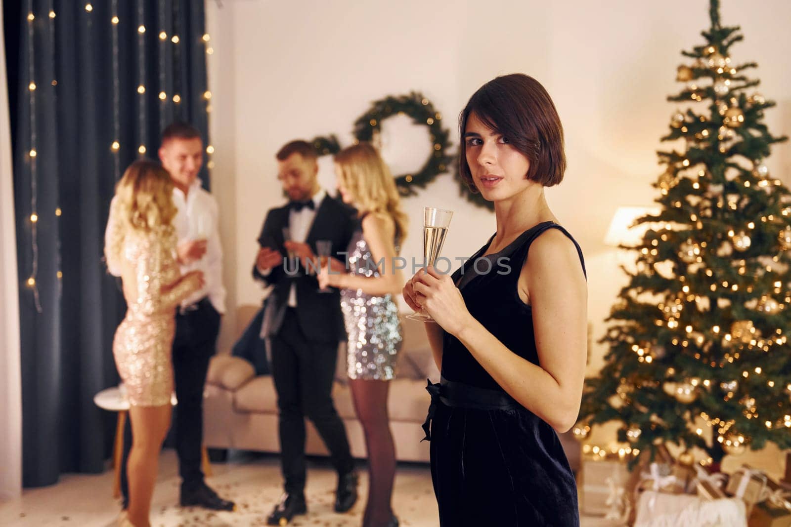 Standing near christmas tree. Group of people have a new year party indoors together.