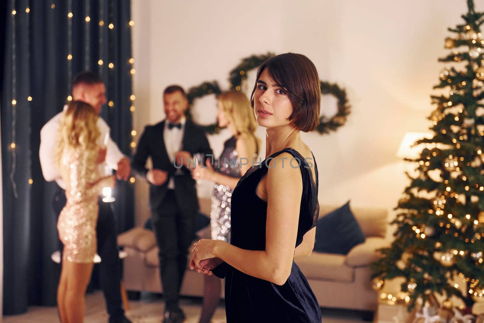 Standing near christmas tree. Group of people have a new year party indoors together.