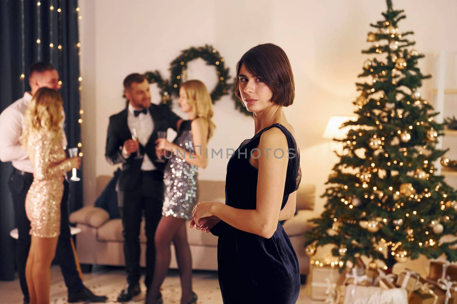 Standing near christmas tree. Group of people have a new year party indoors together.