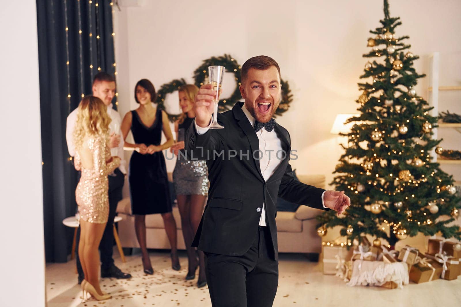 Standing near christmas tree. Group of people have a new year party indoors together.