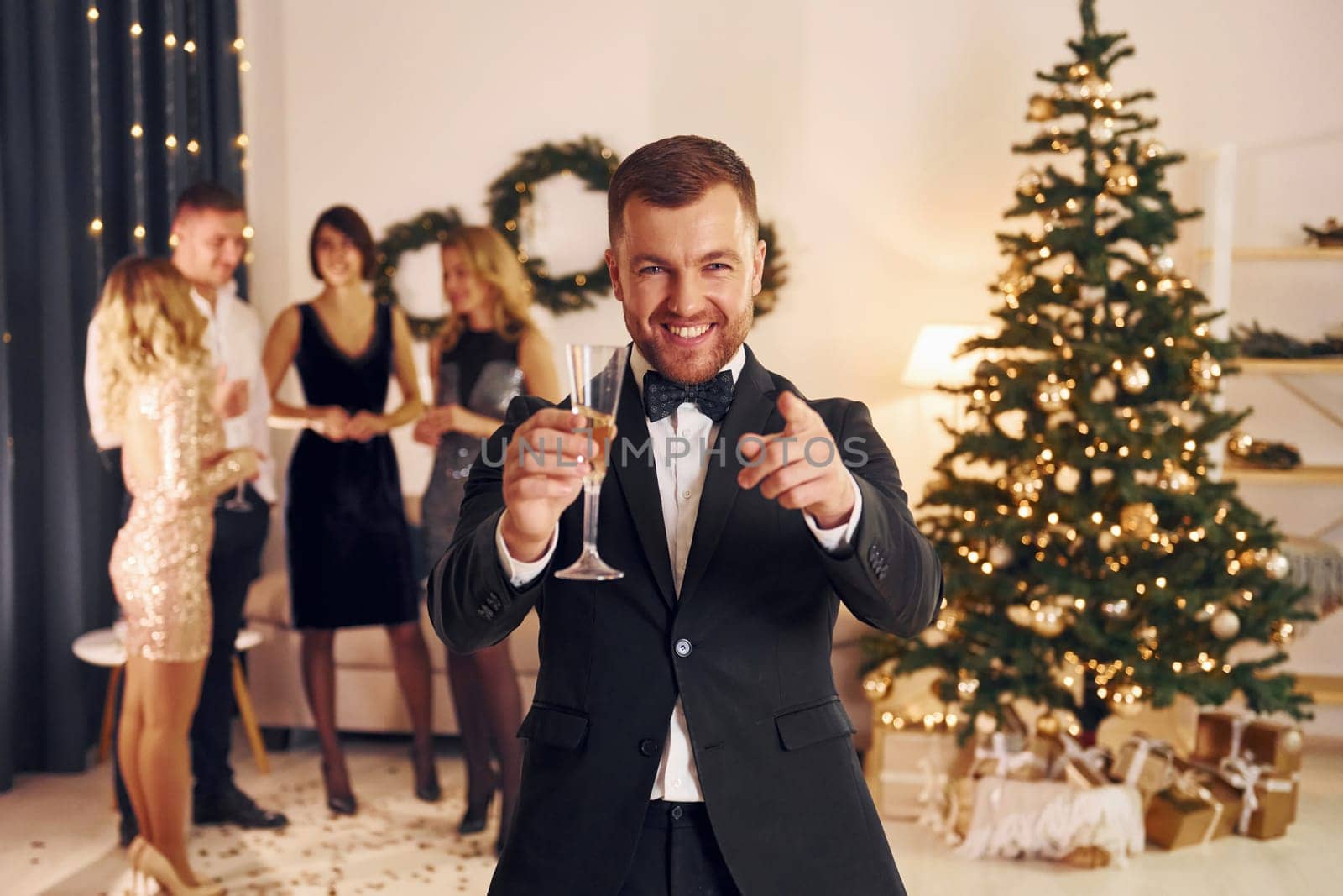 Standing near christmas tree. Group of people have a new year party indoors together.