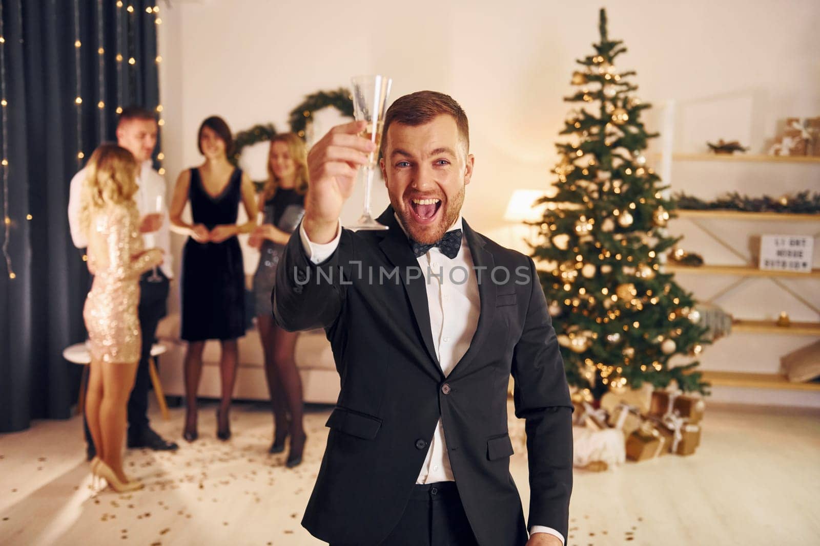 Man with glass of champagne is cheering. Group of people have a new year party indoors together.
