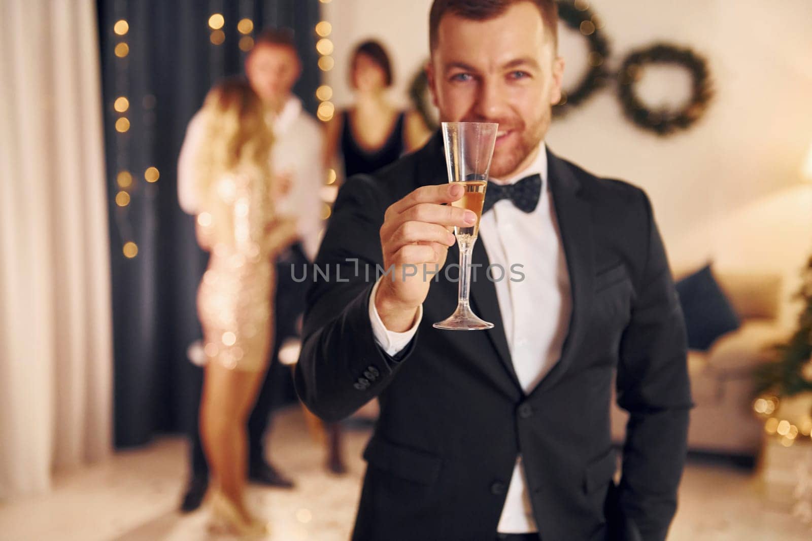 Man with glass of champagne is cheering. Group of people have a new year party indoors together.