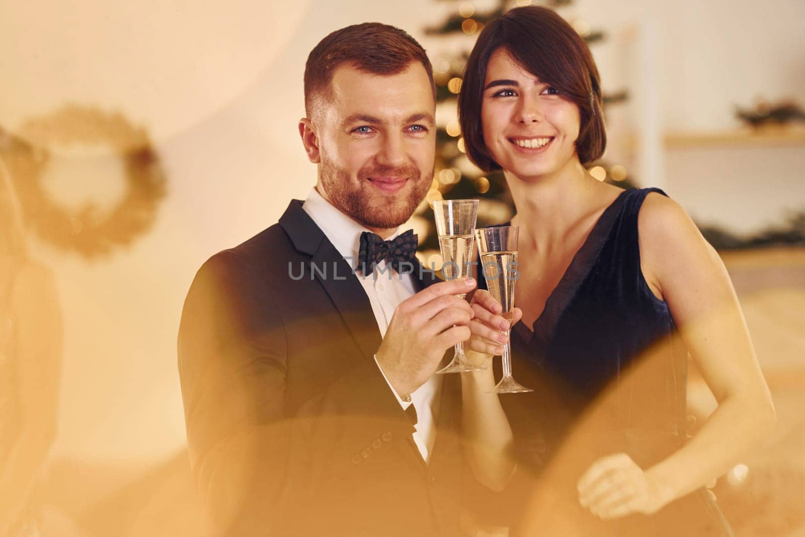 Illuminated by yellow light. Happy couple have a new year party indoors together.