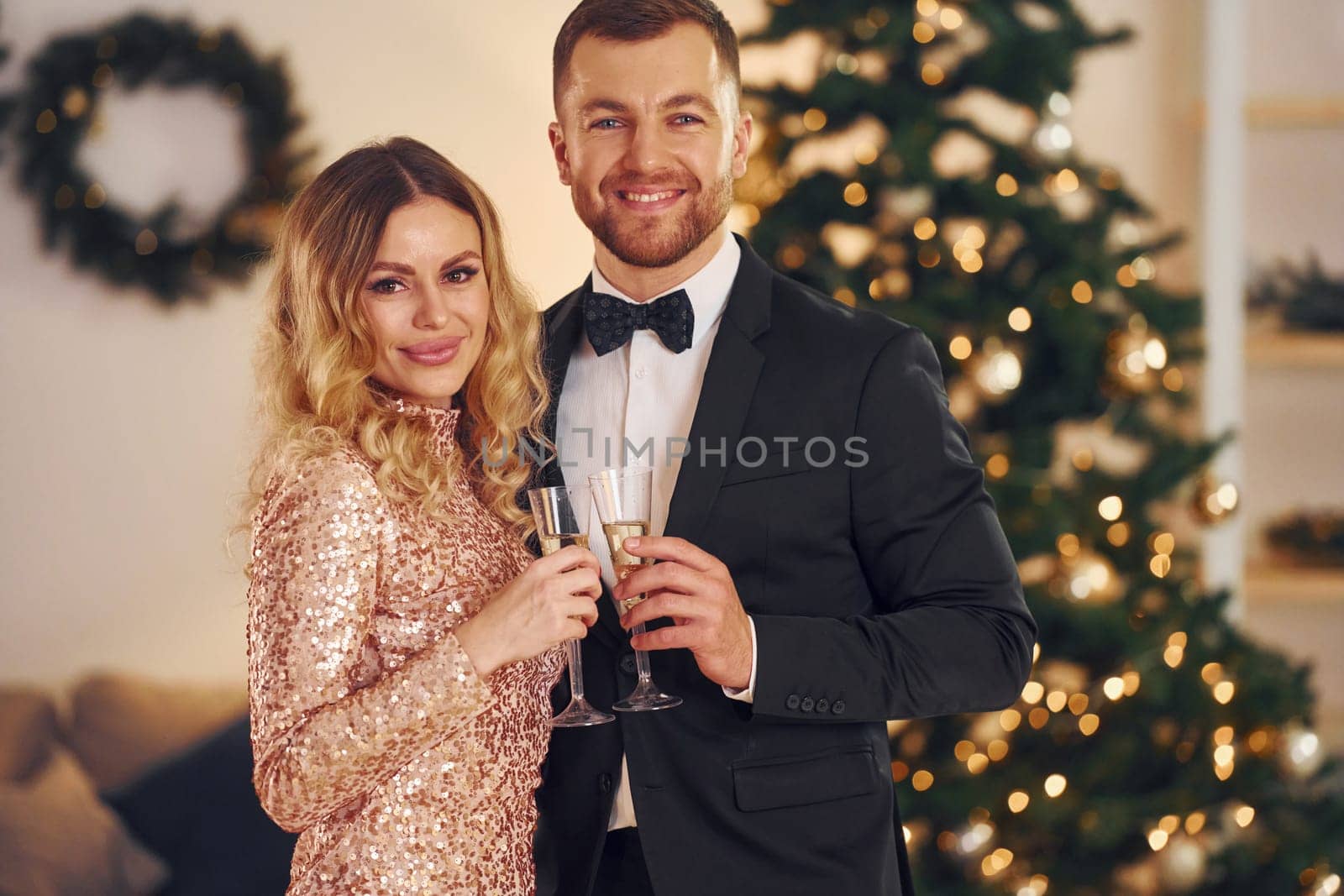 Standing against christmas tree. Happy couple have a new year party indoors together.