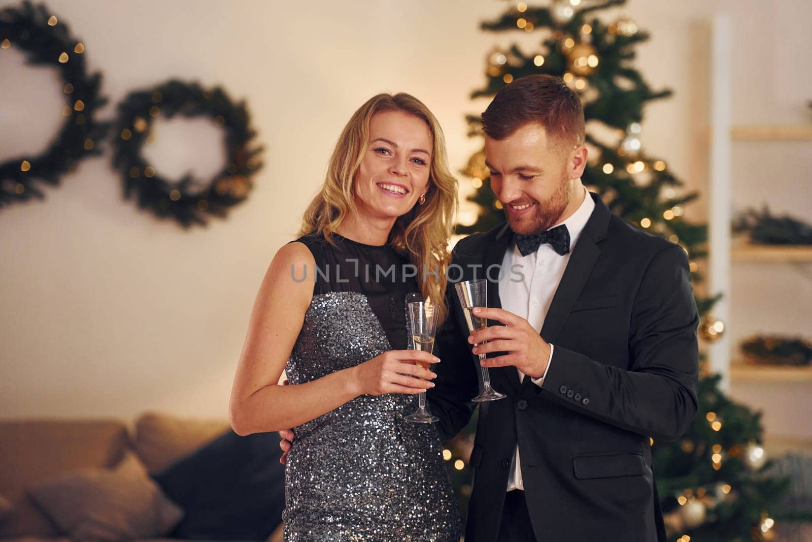 Standing against christmas tree. Happy couple have a new year party indoors together.