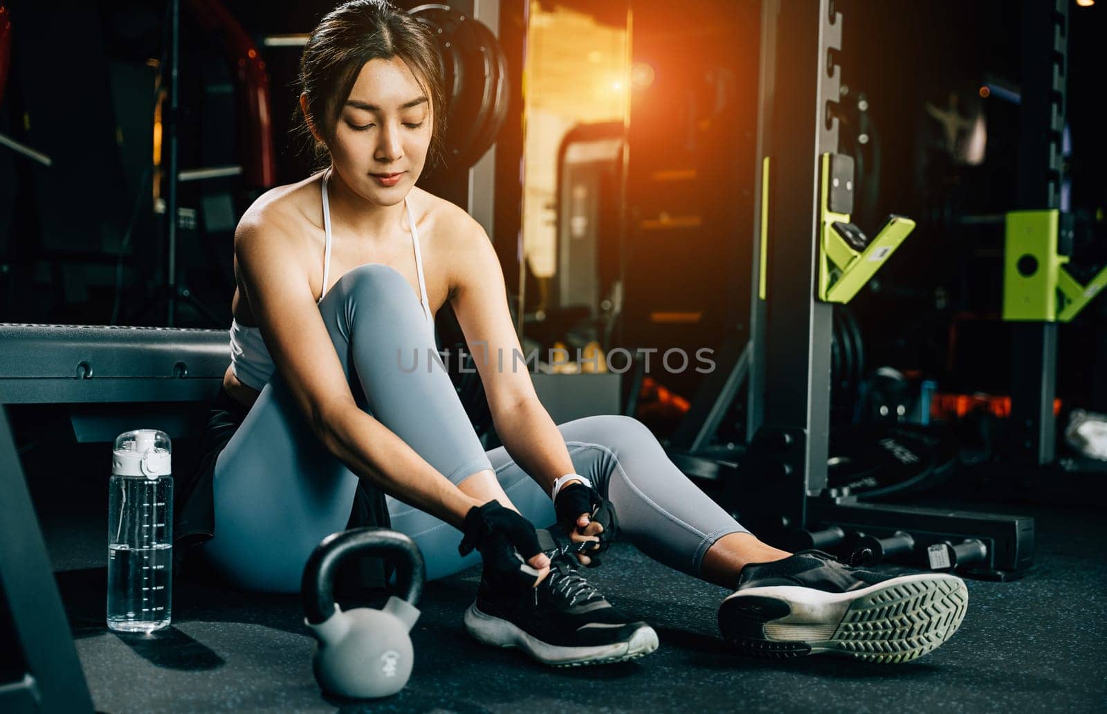 A sportive girl tying her sneakers in preparation for her exercise routine. The shot showcases her stylish shoes and sporty gym pants.