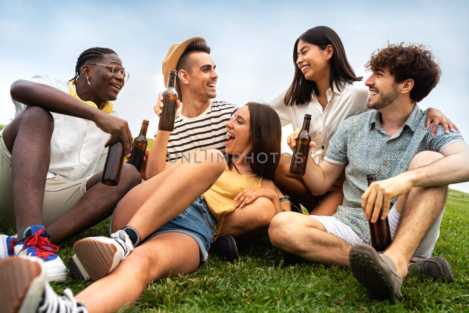 Multiracial friends having fun together drinking beer and laughing outdoors. Friendship concept.
