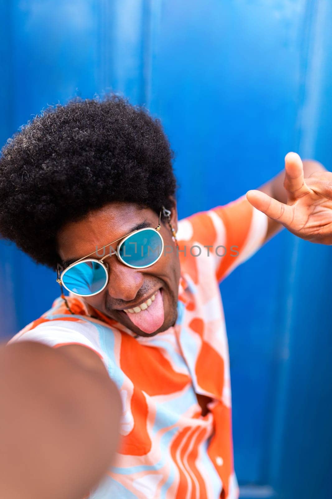 Young African American man with afro hairstyle and sunglasses makes silly faces while taking a selfie with mobile phone. Lifestyle concept.