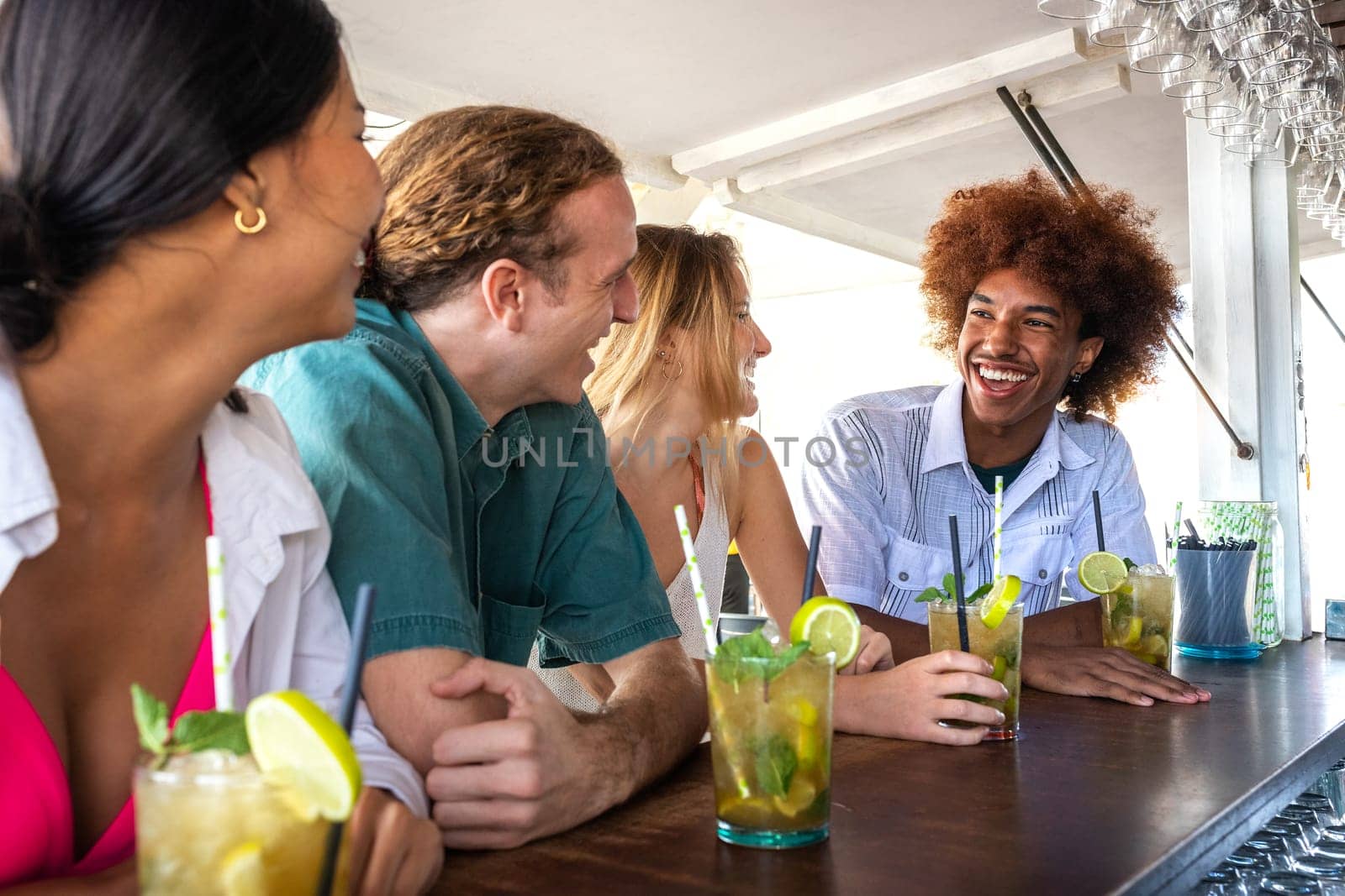 Happy Black young man and his friends enjoying cocktails at beach bar, laughing and having fun. by Hoverstock