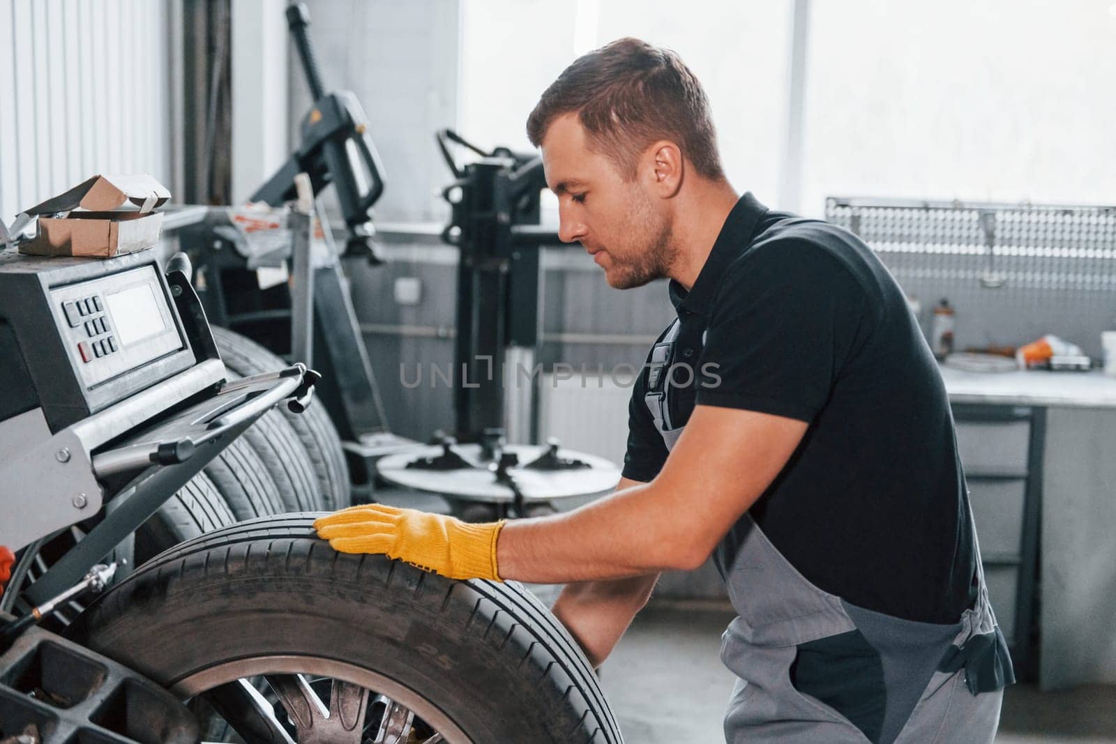 Taking the wheel. Man in uniform is working in the auto service.