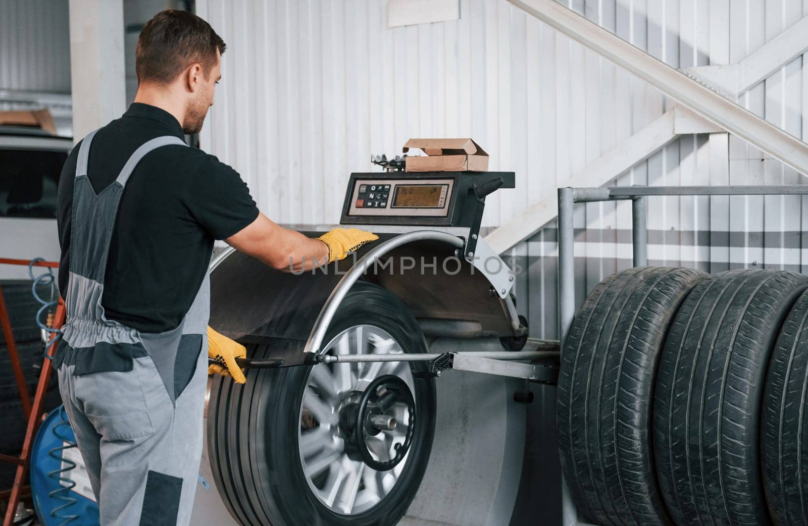 Fixing the tire. Man in uniform is working in the auto service.