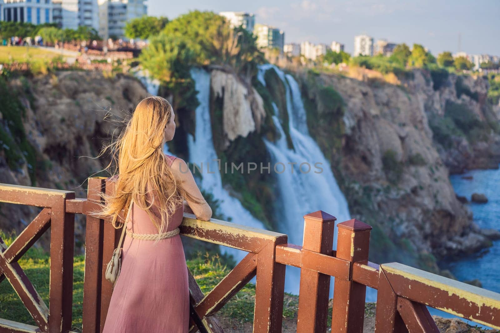 Beautiful woman with long hair on the background of Duden waterfall in Antalya. Famous places of Turkey. Lower Duden Falls drop off a rocky cliff falling from about 40 m into the Mediterranean Sea in amazing water clouds. Tourism and travel destination photo in Antalya, Turkey. Turkiye.