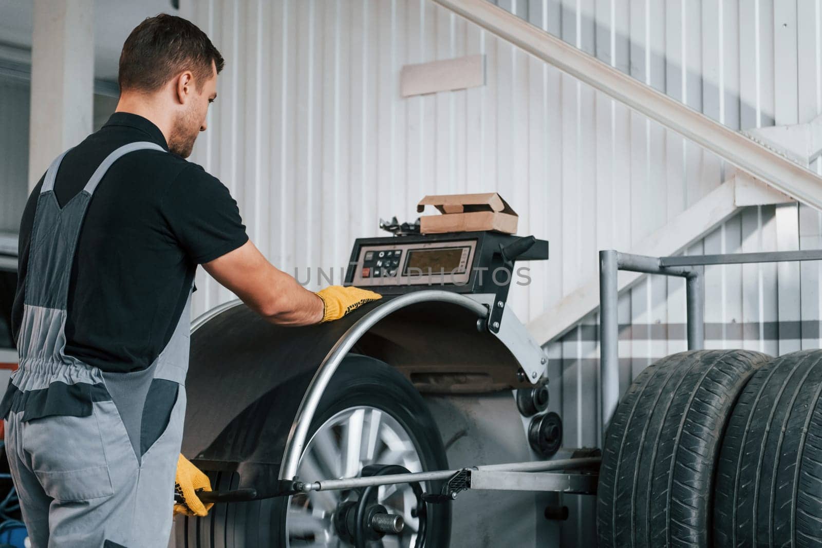 Fixing the tire. Man in uniform is working in the auto service.