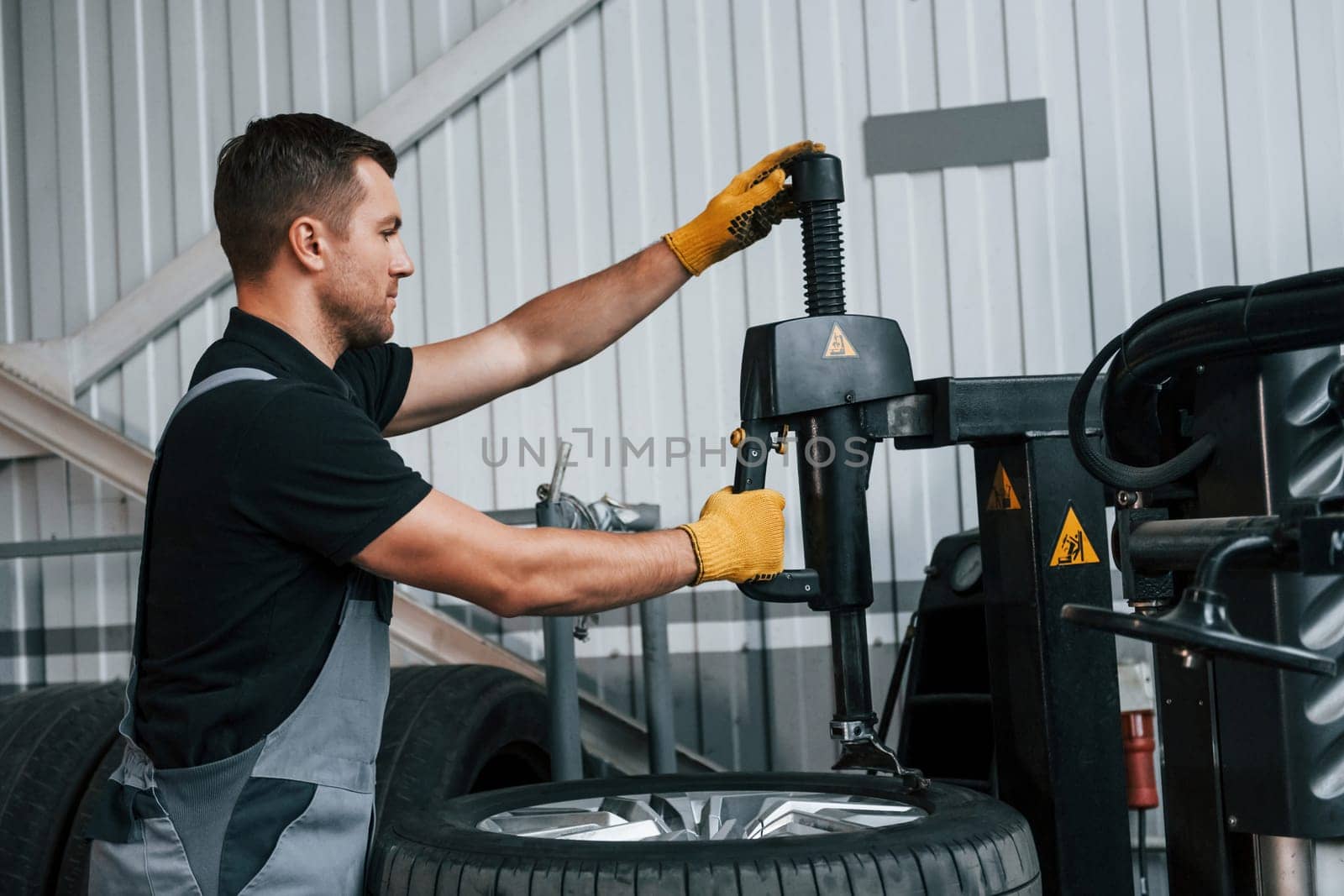 Fixing the tire. Man in uniform is working in the auto service.