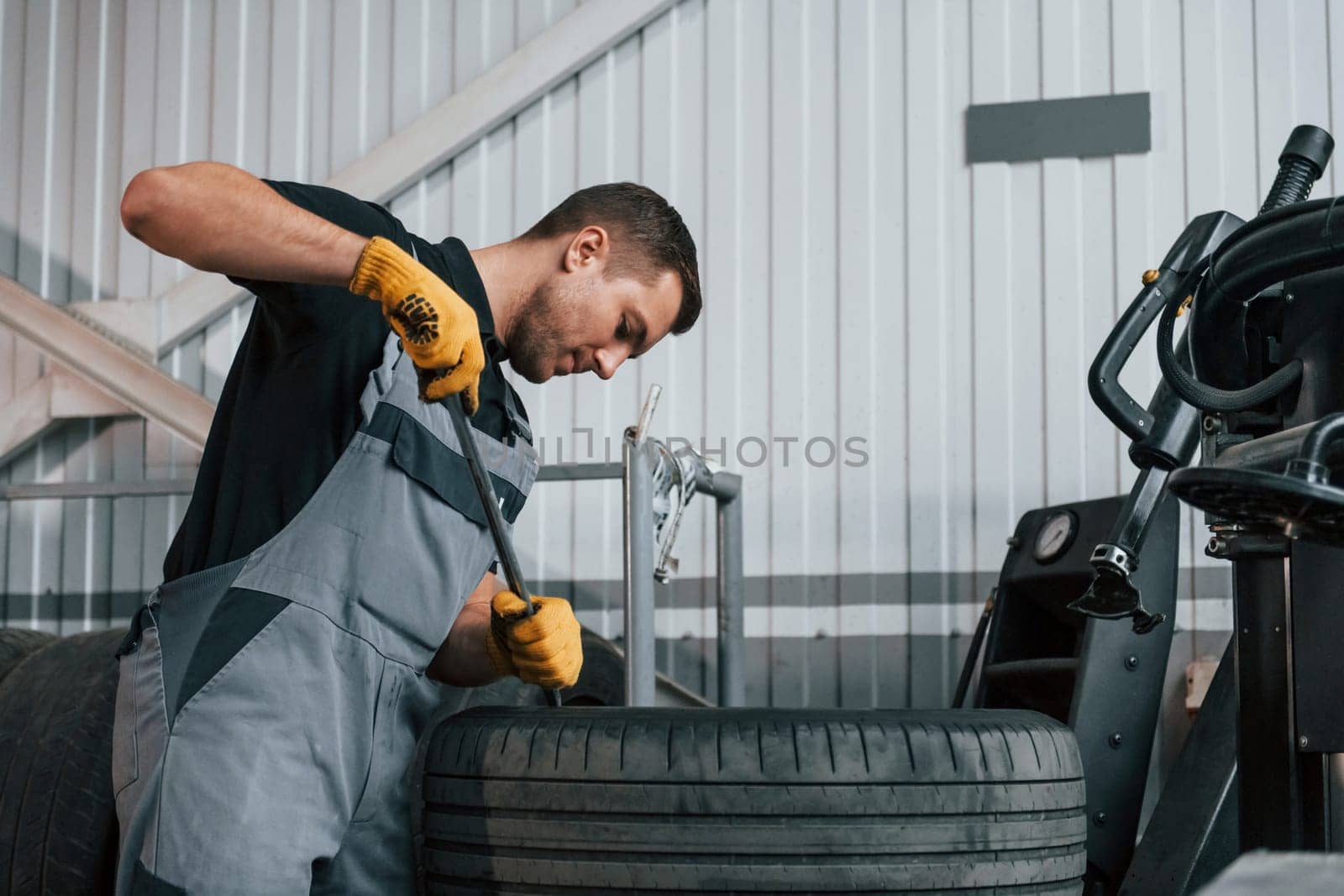 Working with broken wheel. Man in uniform is working in the auto service.