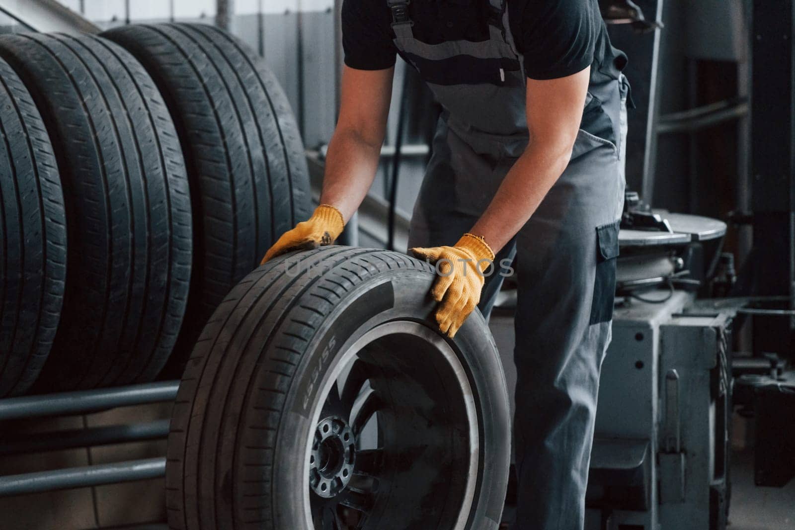 Walking with tyre. Man in uniform is working in the auto service.