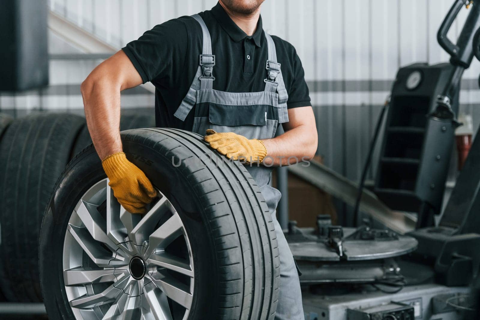 Walking and holding tyre. Man in uniform is working in the auto service.