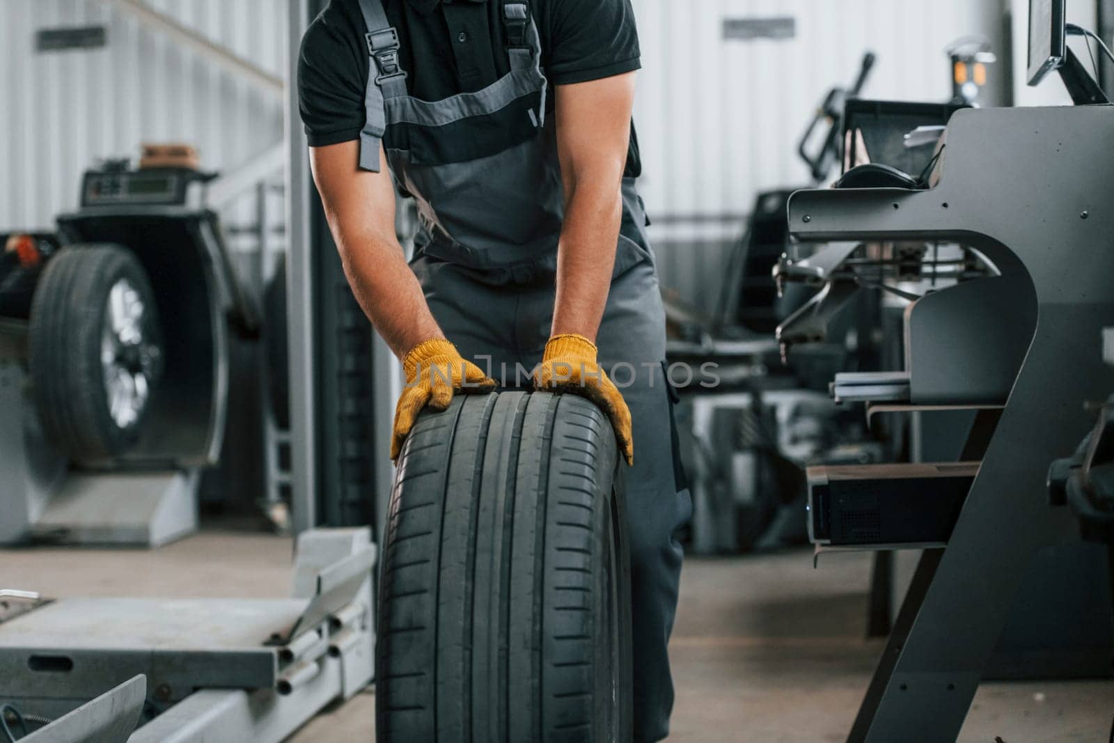 Close up view of wheel. Man in uniform is working in the auto service.