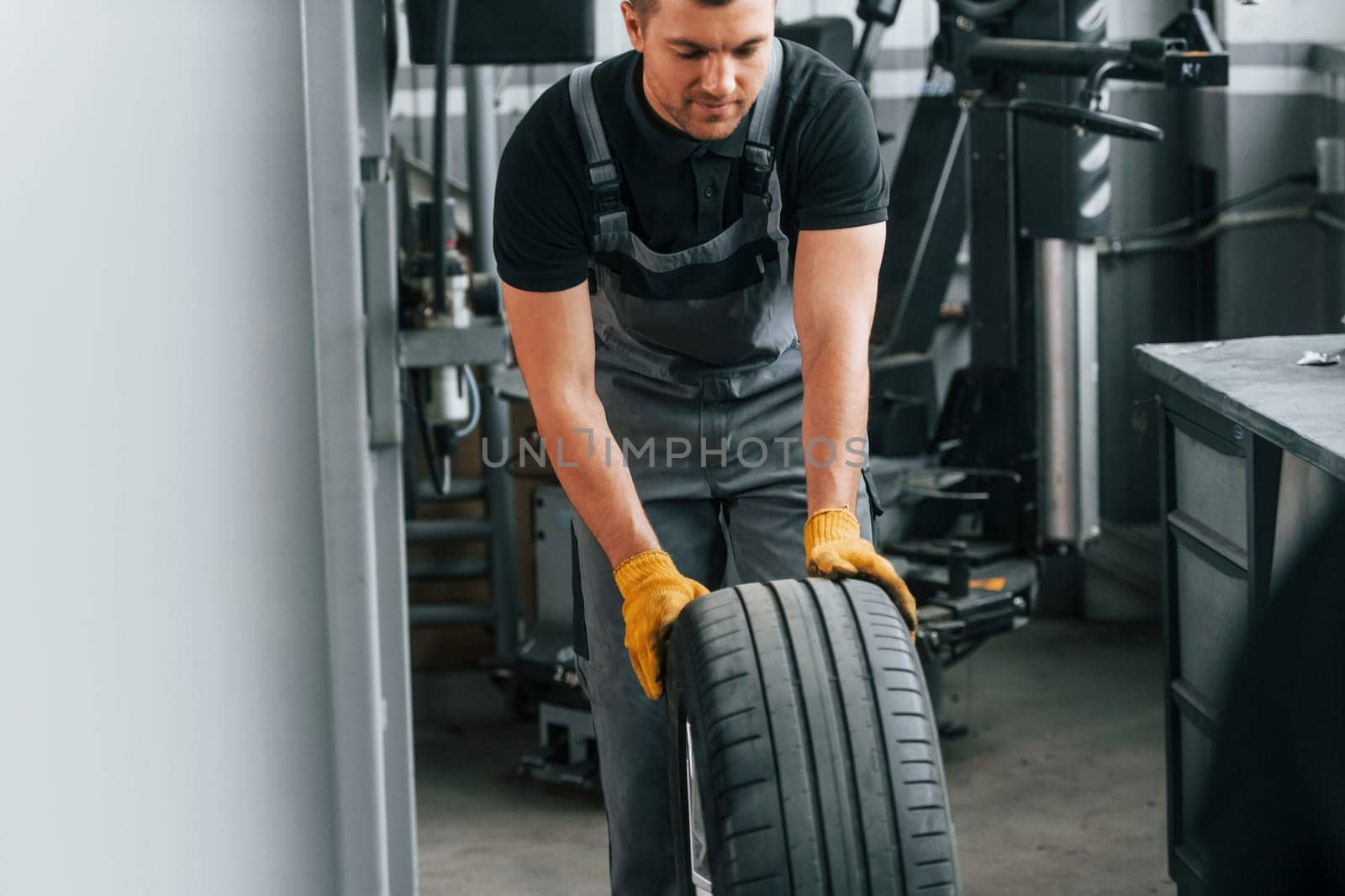 Close up view of wheel. Man in uniform is working in the auto service by Standret