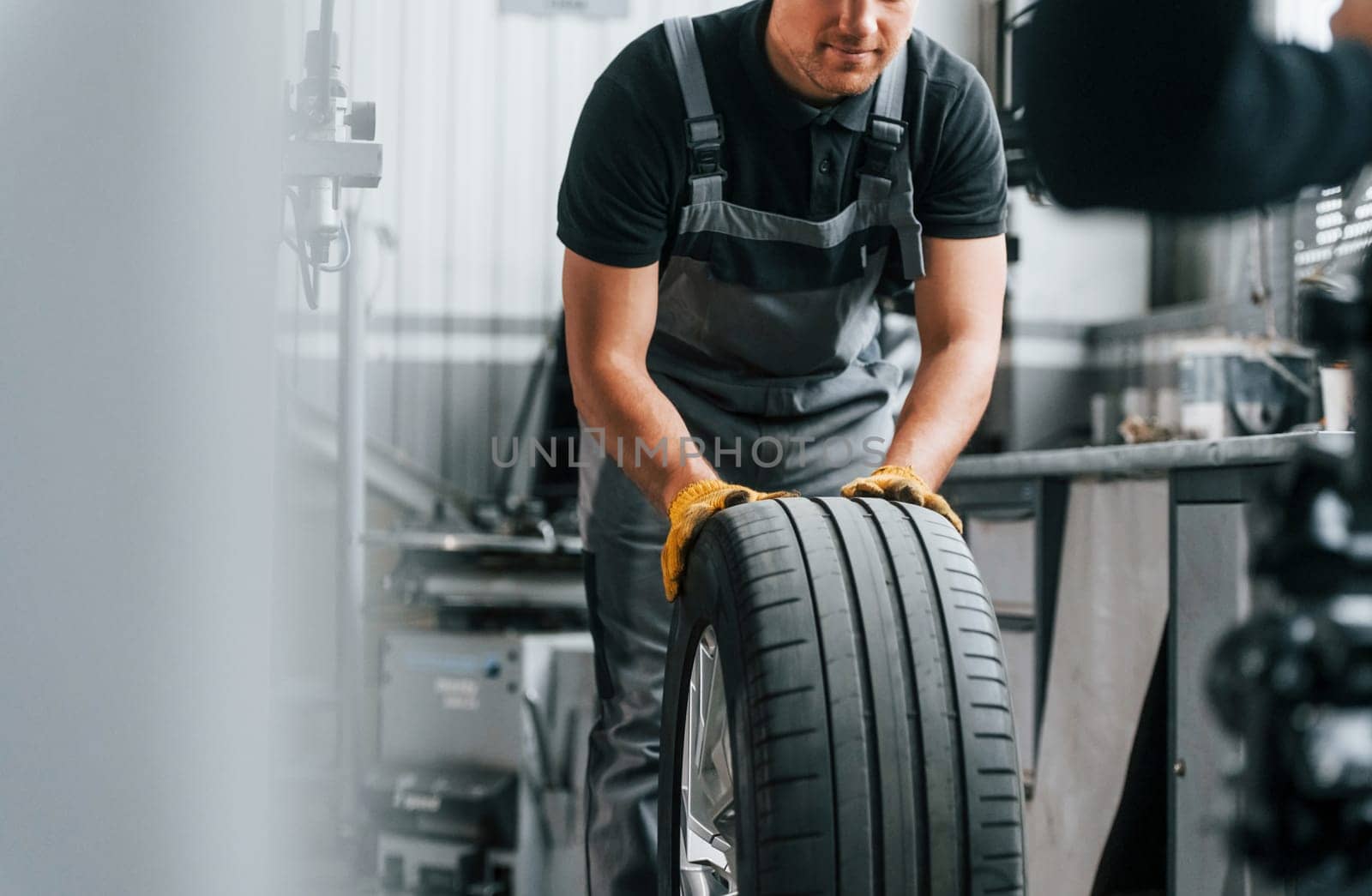 Close up view of wheel. Man in uniform is working in the auto service.